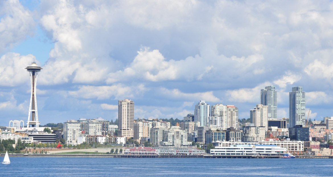 Seattle skyline and Space Needle seen across Elliott Bay under white clouds and blue sky