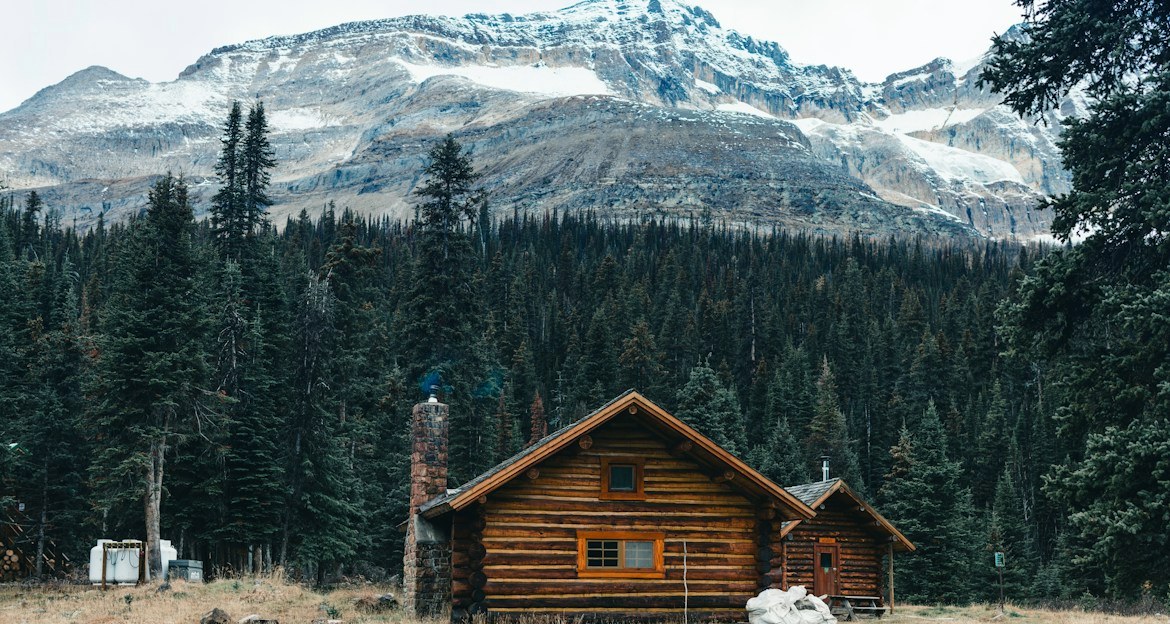 Secluded log cabin in a pine forest below snowy peaks, a classic base for romantic mountain getaways