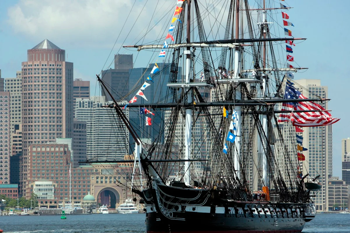 USS Constitution sailing in Boston Harbor with the city skyline behind